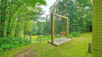 A wooden swing set in a lush green garden with a pond in the background.