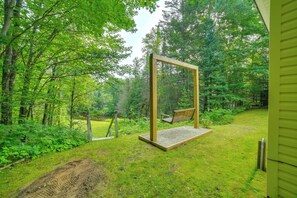 Un'altalena di legno in un rigoglioso giardino verde con uno stagno sullo sfondo.