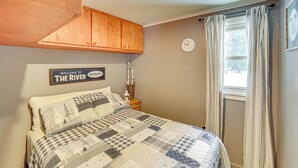 A bedroom with a bed, a wooden cabinet, a clock, and a window with curtains. - Fish, Hike & Relax: Riverfront Manistique Cabin (Manistique)