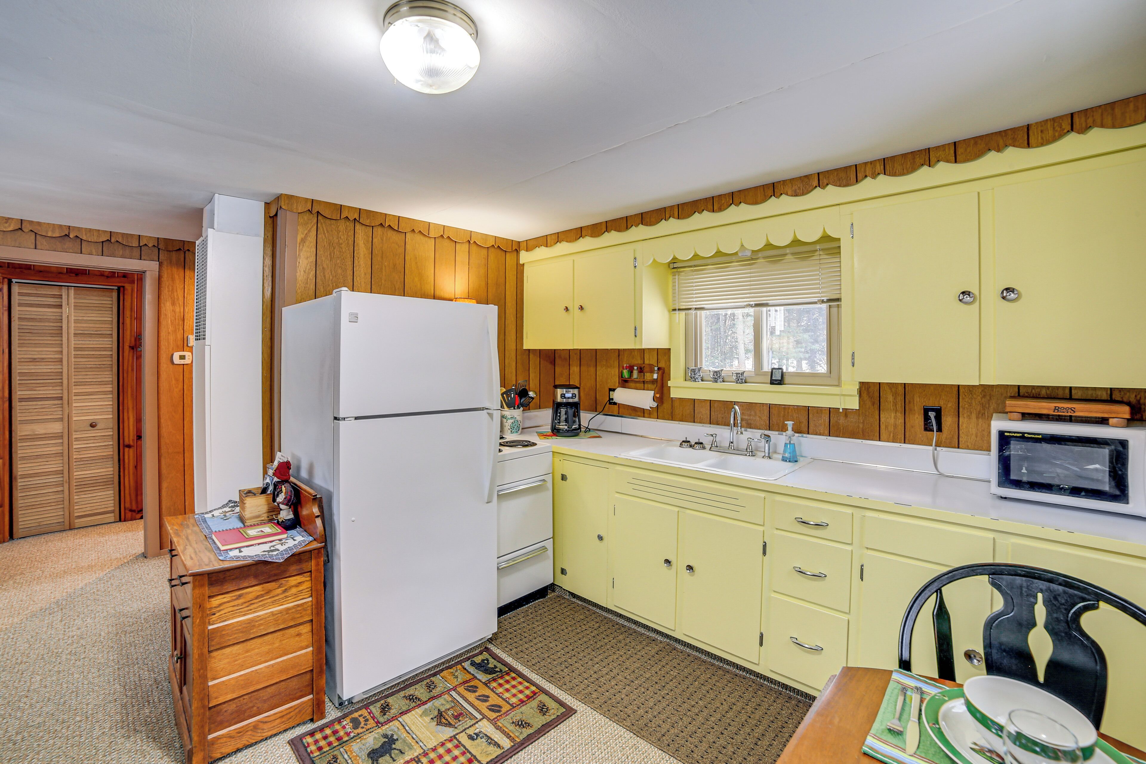A compact kitchen with wooden cabinets, a refrigerator, a microwave, and a sink.