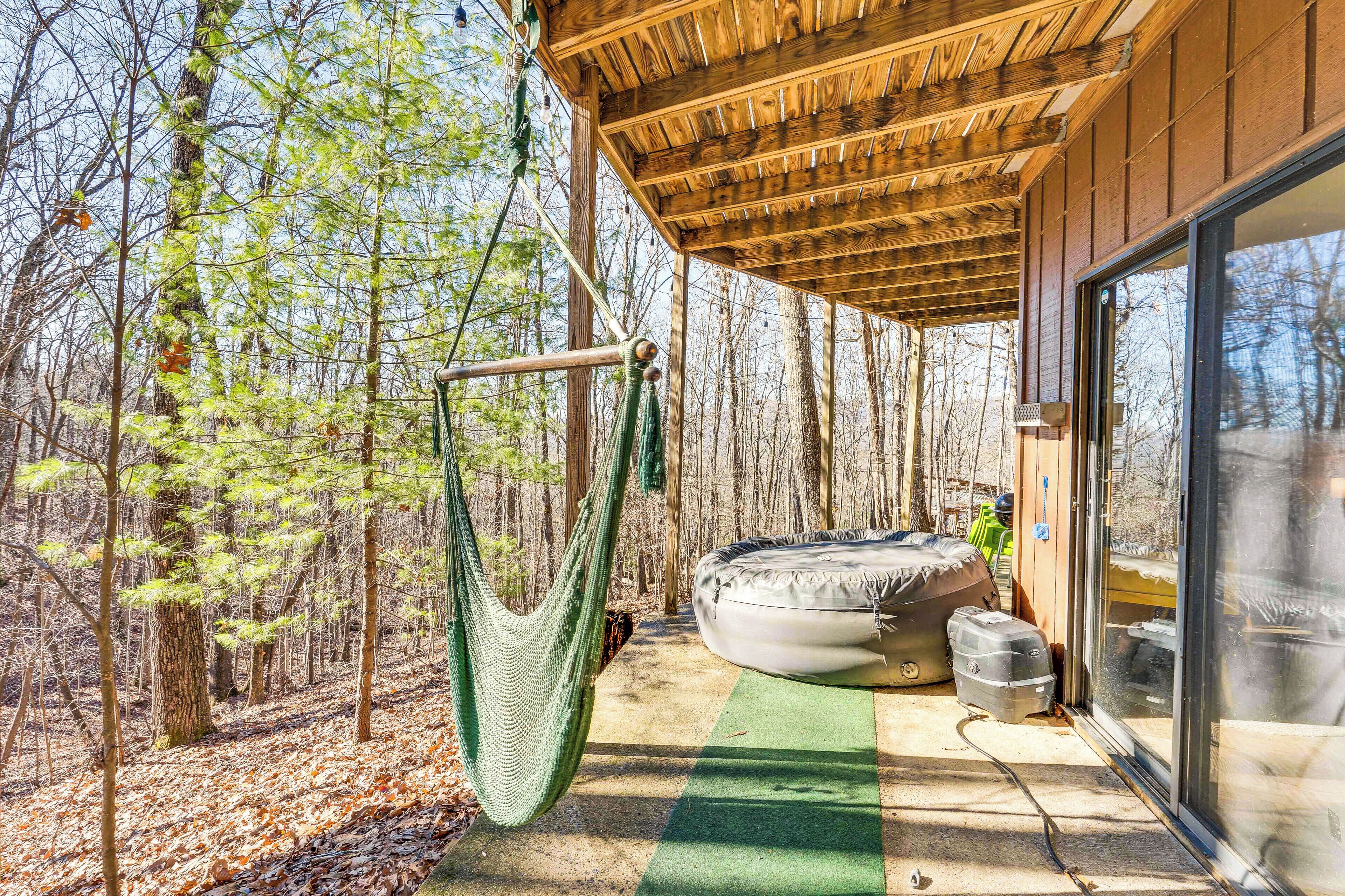 A covered outdoor area with a hammock, a hot tub, and a glass door leading to a forested area.