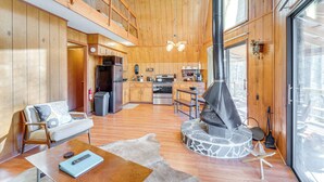 A spacious living area with a high ceiling, wooden walls, a stone fireplace, and a kitchen with modern appliances. - Hot Tub, Deck & Fire Pit: Secluded Cabin in Murphy (Murphy)