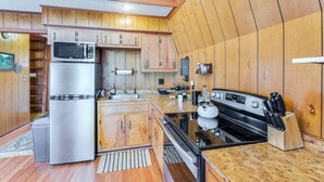 A compact kitchen with wooden cabinets, a stainless steel refrigerator, a stove, and a sink. - Hot Tub, Deck & Fire Pit: Secluded Cabin in Murphy (Murphy)