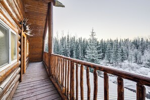 A wooden balcony with a railing, a window, and a view of snow-covered trees. - 3 Mi to Kenai River: Secluded Sterling Cabin! (Sterling)