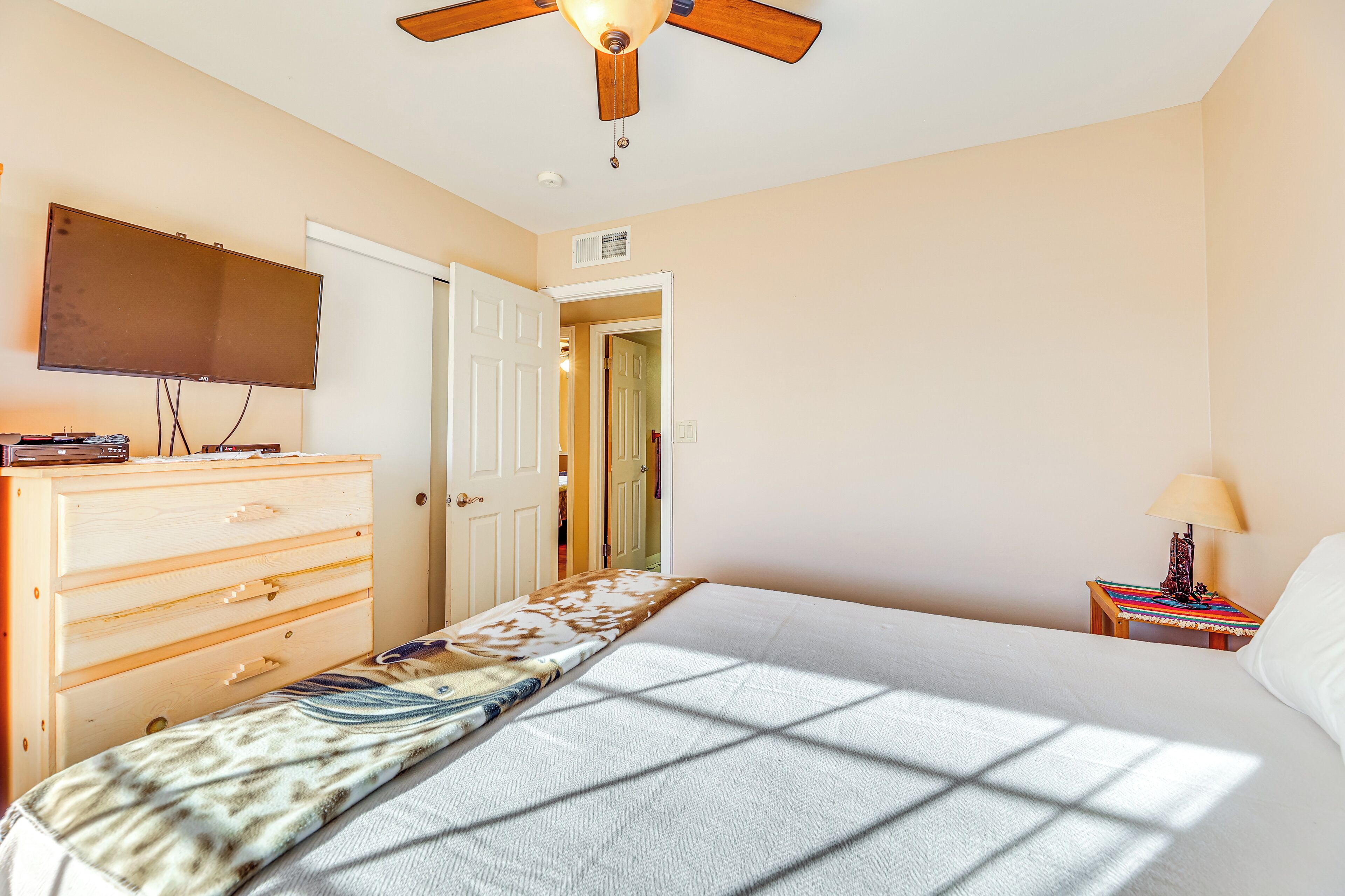 A bedroom with a bed, a dresser, a television, a ceiling fan, and a nightstand with a lamp.