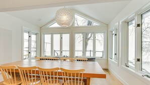 A spacious dining area with a large wooden table and four wooden chairs, large windows with a view of the outdoors, and a unique hexagonal pendant light. - Lake Wisconsin Retreat w/ Dock: Great for Groups! (Lodi)