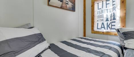 Ein Schlafzimmer mit zwei Betten, einer Holzbalkendecke, einem gerahmten Bild und einem Fenster mit dem Schriftzug 'Das Leben am See ist besser'.