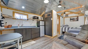 Cocina compacta con refrigerador, microondas y armarios de madera. Cuenta con una mesa de comedor con sillas y un sofá en la zona de estar.