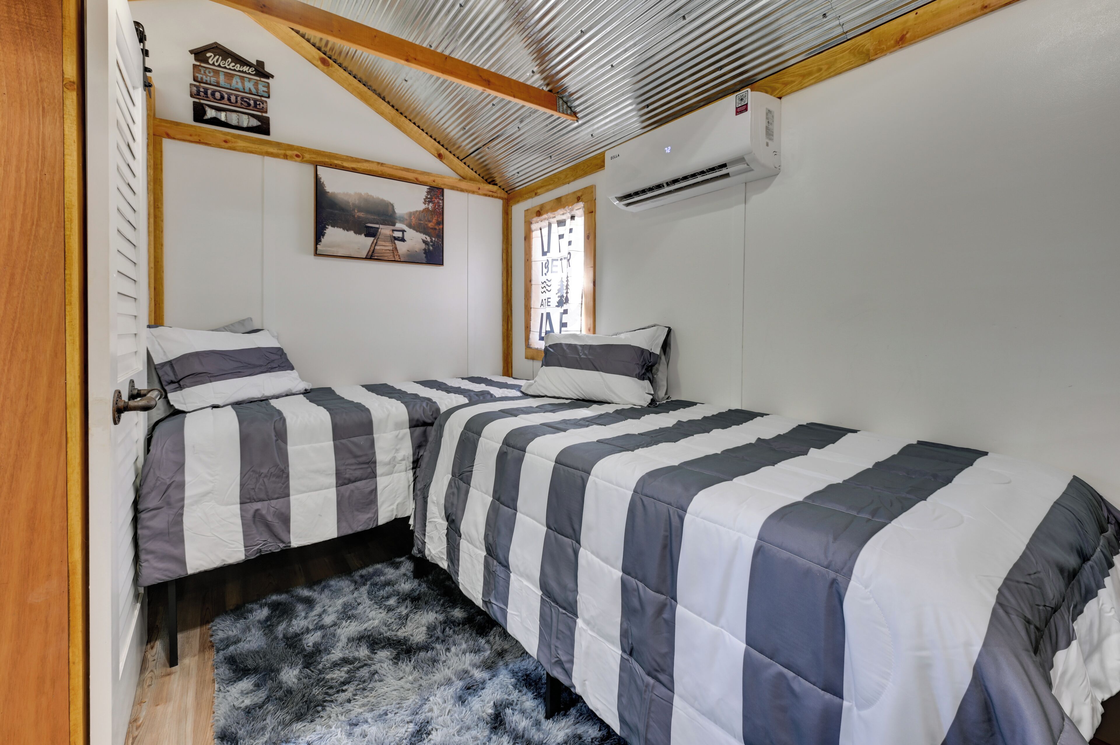 Un dormitorio con dos camas, techo de madera, un cuadro y un cartel de bienvenida.