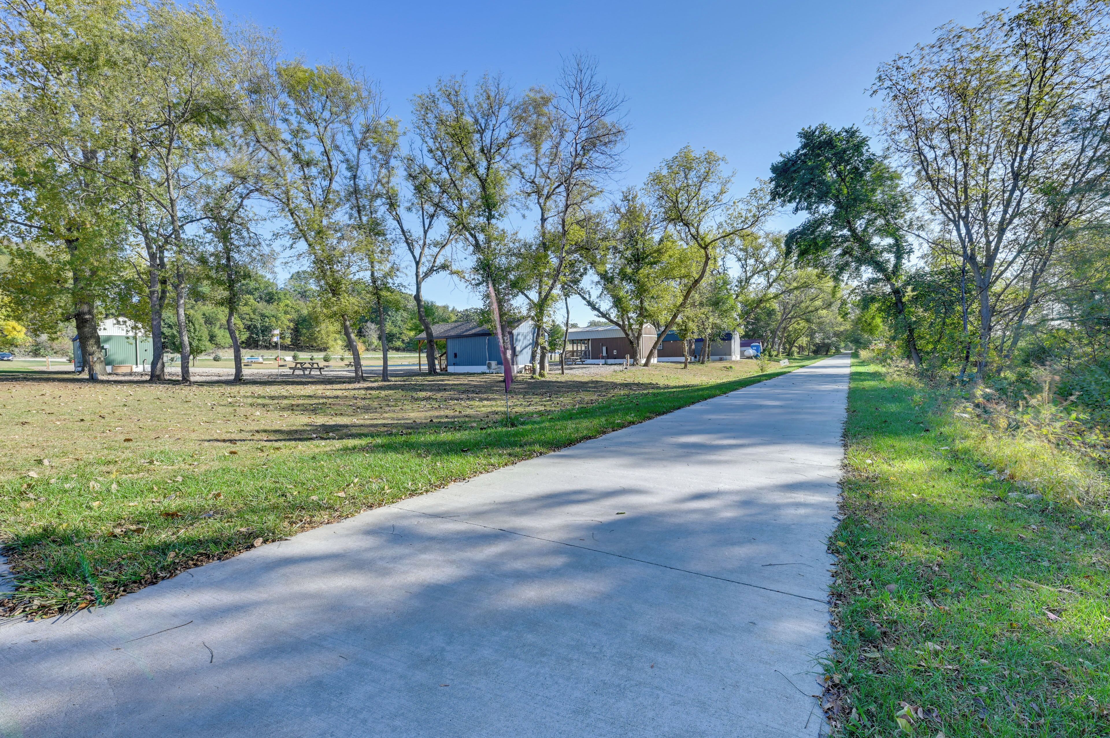 A paved pathway flanked by trees and grassy areas, leading to a building with a blue roof.