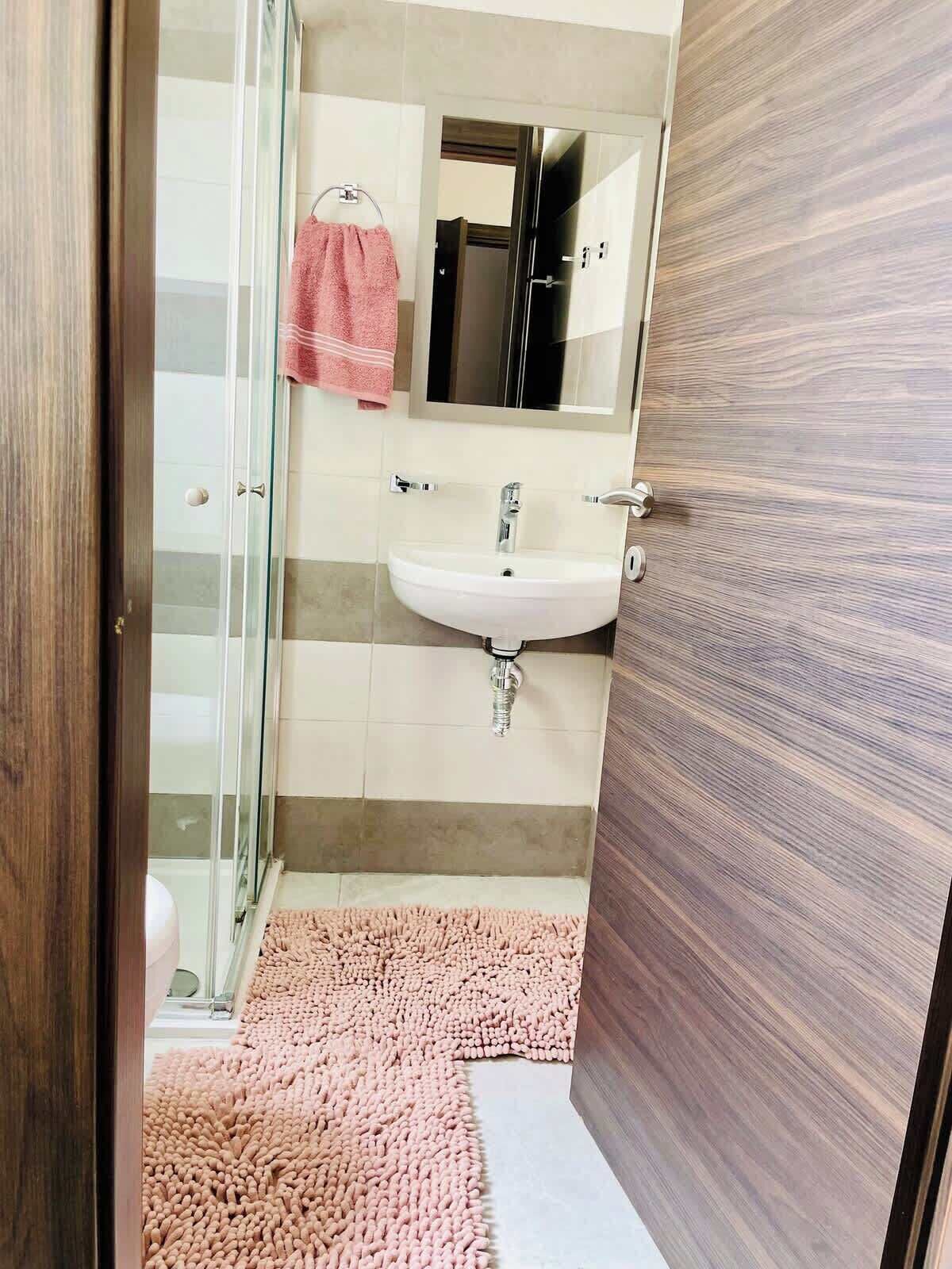 A bathroom with a glass shower enclosure, a white sink, and a mirror above it.