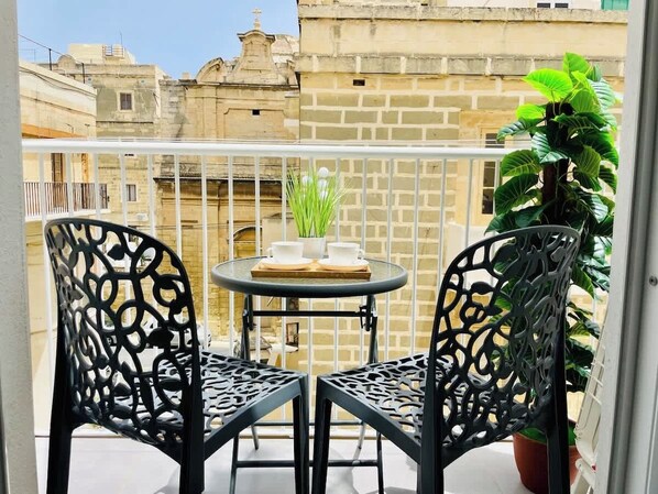 A balcony with two black metal chairs, a small round table, and a potted plant.