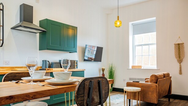 A modern kitchen with green cabinets, a wooden dining table, and a comfortable seating area with a sofa and chairs. - WhiskAwayStays No. 58 Studio No. 6 (Worcester)