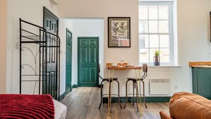 A room with a bed, a table with chairs, a window with a plant, and a green door. - WhiskAwayStays No. 58 Studio No. 6 (Worcester)