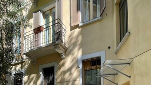 A courtyard with a cobblestone path, a yellow building with multiple windows and balconies, and a small garden area.