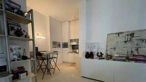 A modern kitchen with white cabinetry, a dining area with a table and chairs, and a bookshelf filled with books and decorative items.