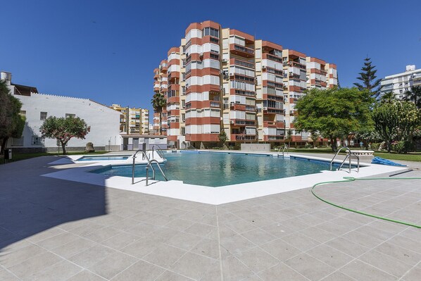 Una piscina con solárium empinado, rodeada por un edificio residencial de varios pisos con balcones.