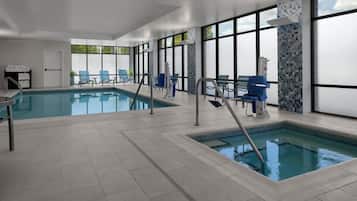 An indoor swimming pool with clear water, surrounded by blue chairs and a tiled floor.