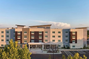 A modern hotel with a central entrance, multiple floors, and a parking lot.