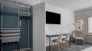 Une chambre moderne équipée d’un bureau, de chaises, d’un téléviseur, d’un porte-manteau et d’une fenêtre.