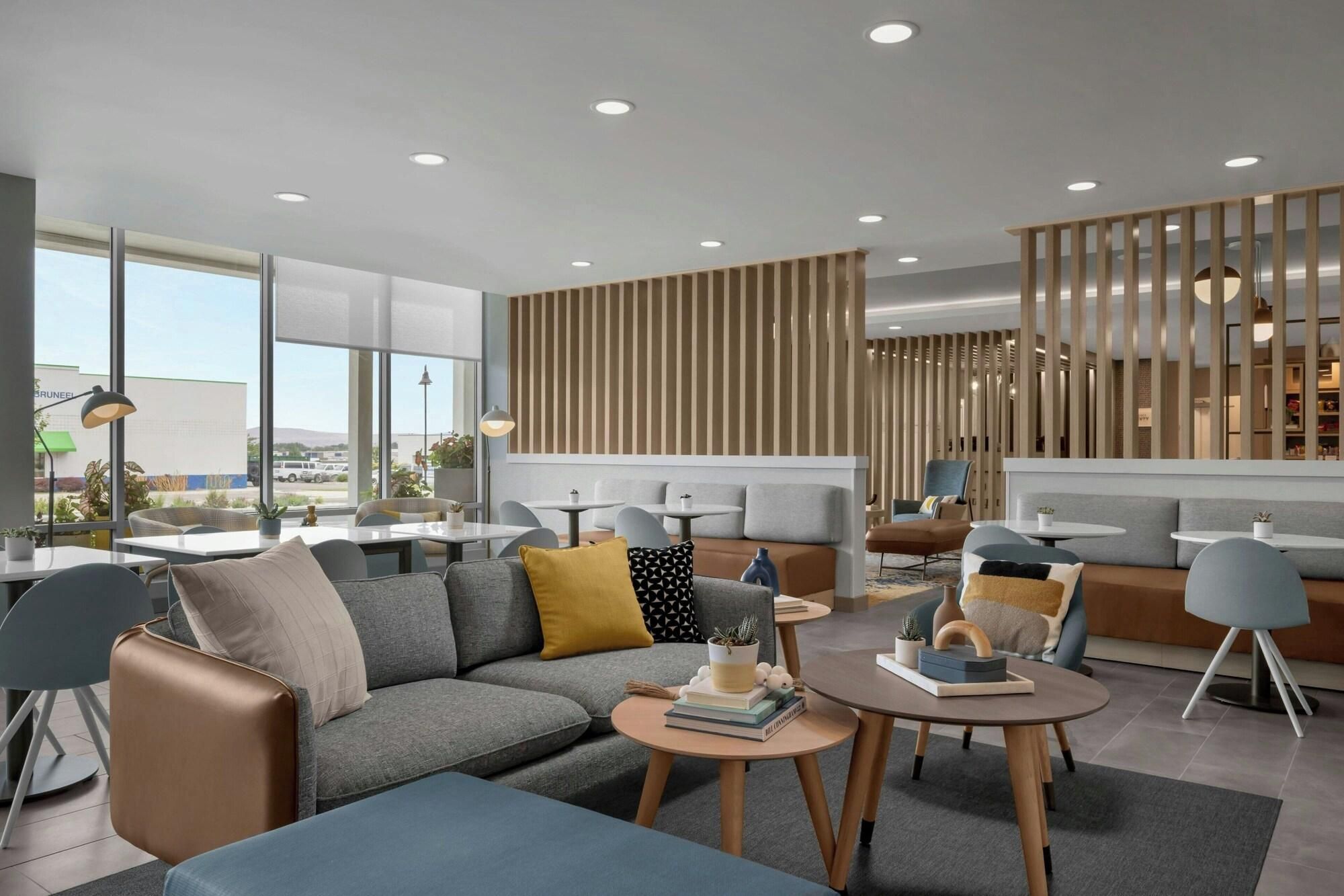 A modern hotel lobby with a sectional sofa, round tables, and a vertical wooden panel wall.