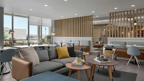 A modern hotel lobby with a sectional sofa, round tables, and a vertical wooden panel wall. - Towneplace Suites By Marriott Nampa (Nampa)