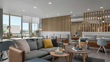 A modern hotel lobby with a sectional sofa, round tables, and a vertical wooden panel wall.