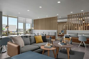 Un moderno hall de hotel con un sofá modular, mesas redondas y un panel de pared de madera vertical.