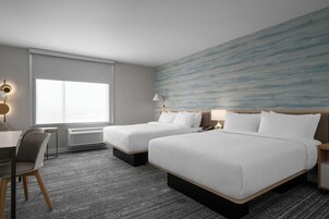 Habitación de hotel con dos camas, un escritorio, una silla y un ventanal grande.