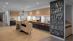 Une cuisine moderne avec des meubles en bois, un îlot central, des luminaires suspendus et un panneau d’affichage en forme d’ardoise.