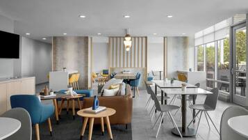 A modern hotel lobby with a sofa, chairs, tables, and a TV screen.