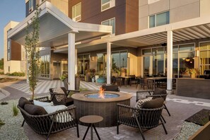 Un espace extérieur moderne, aménagé avec des fauteuils en osier, un foyer central et une terrasse couverte.