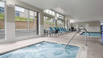 A modern indoor swimming pool with clear windows, lounge chairs, and a poolside area.