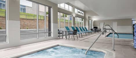 Una piscina interior moderna con ventanales amplios, sillas de descanso y una zona de borde de piscina.