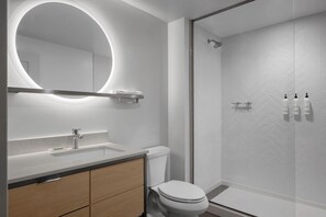 Un bagno moderno con uno specchio rotondo, un water, una doccia e un lavabo.