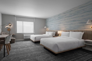Habitación de hotel con dos camas, un escritorio, una silla, una ventana y una pared con diseño texturizado.