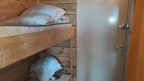 Um pequeno quarto de madeira com duas beliches e uma porta.