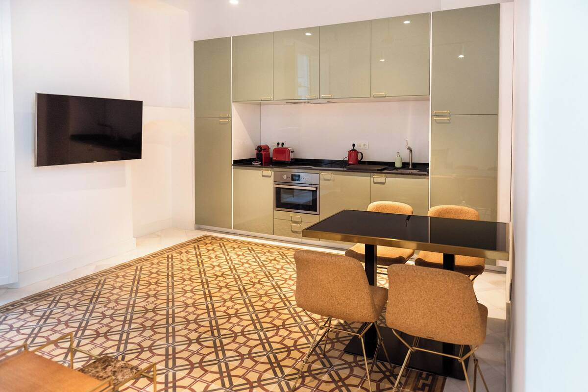 A modern kitchen with a flat-screen TV, a dining area with a patterned floor, and a small oven.