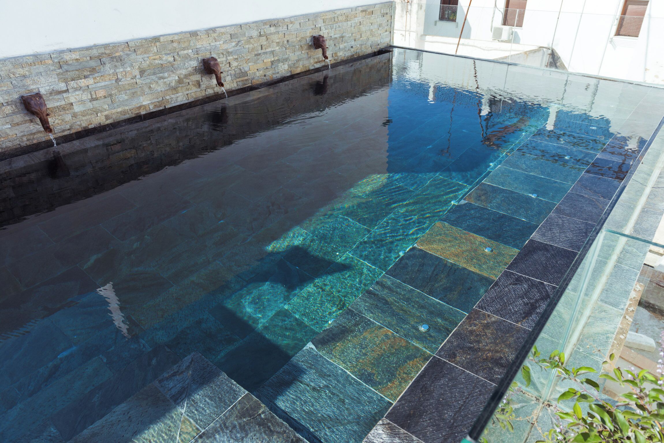 Una piscina cristalina con un muro de piedra y borde de vidrio.