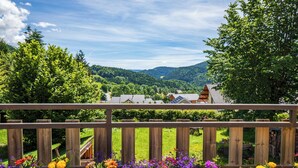 A wooden deck with a view of a village, surrounded by lush greenery and hills. - Apartment Les Roses du Vercors Panoramic view (Villard-de-Lans)