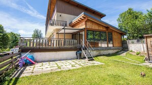 A two-story wooden house with a balcony, a covered patio, and a small garden area. - Apartment Les Roses du Vercors Panoramic view (Villard-de-Lans)