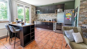A modern kitchen with dark cabinets, a central island, and a dining area with two chairs. - Apartment Les Roses du Vercors Panoramic view (Villard-de-Lans)
