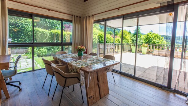 A spacious room with a large wooden table and chairs, large windows, and a view of a garden. - Apartment Les Roses du Vercors Panoramic view (Villard-de-Lans)