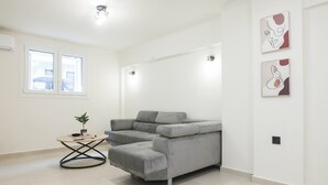 Un salon moderne avec un canapé d’angle gris, une petite table ronde ornée d’une plante et deux tableaux abstraits accrochés au mur.