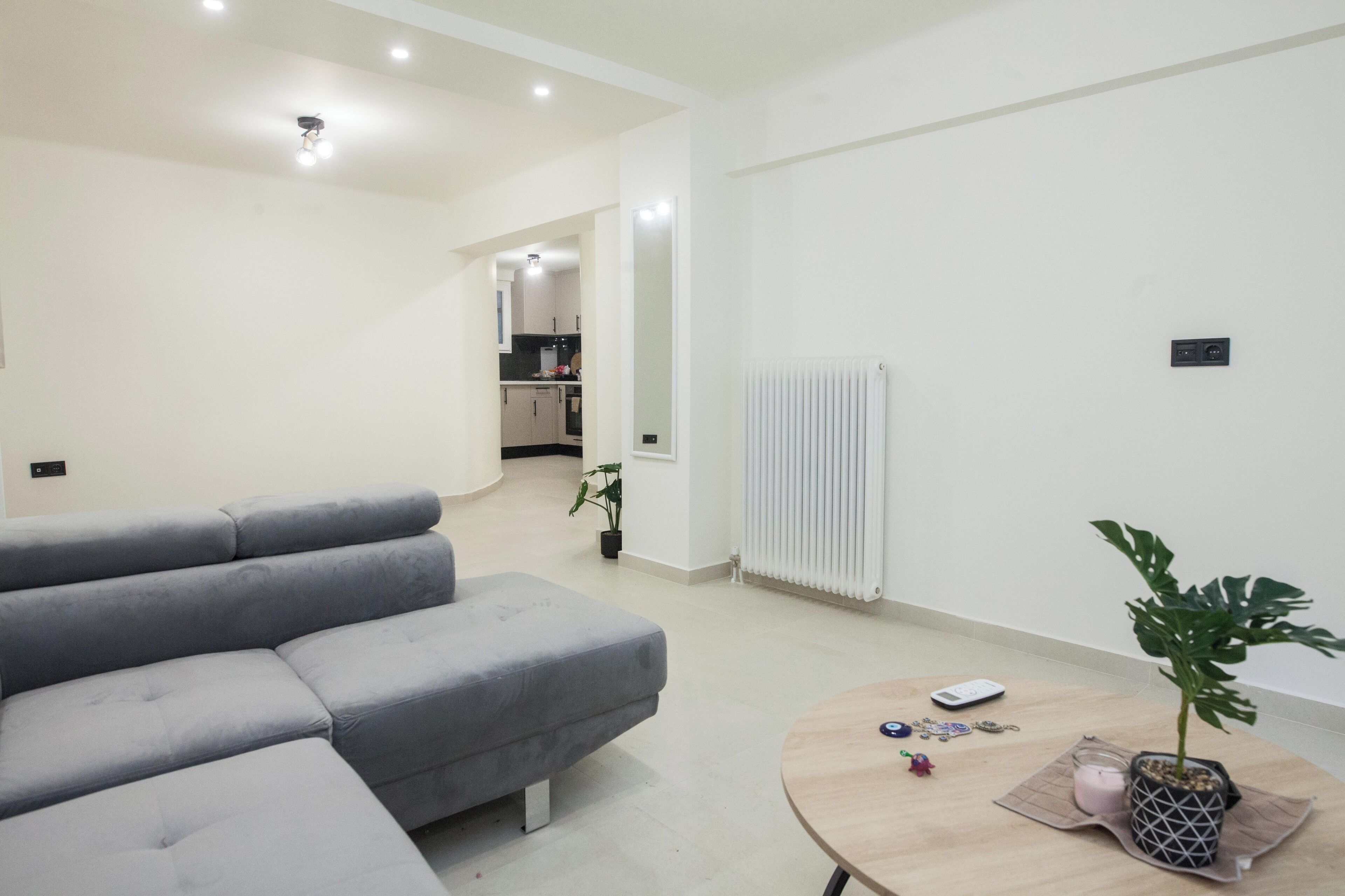 Een moderne woonkamer met een grijze modulaire bank, een ronde houten salontafel en een potplant.