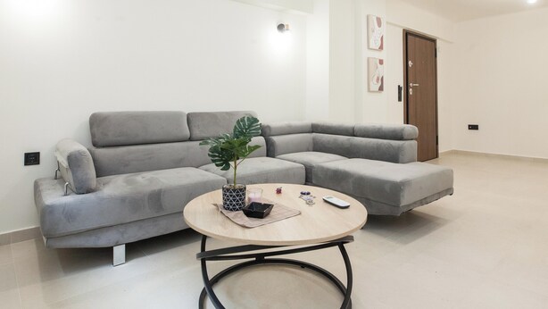 Un salon moderne avec un canapé d’angle gris, une table basse ronde et une plante en pot.