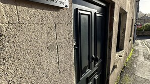 En byggnadsfasad med en svart dörr och en skylt med texten ”27 Acre Street”.