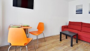 Une pièce avec un canapé rouge, des fauteuils orange, une petite table et un téléviseur fixé au mur.