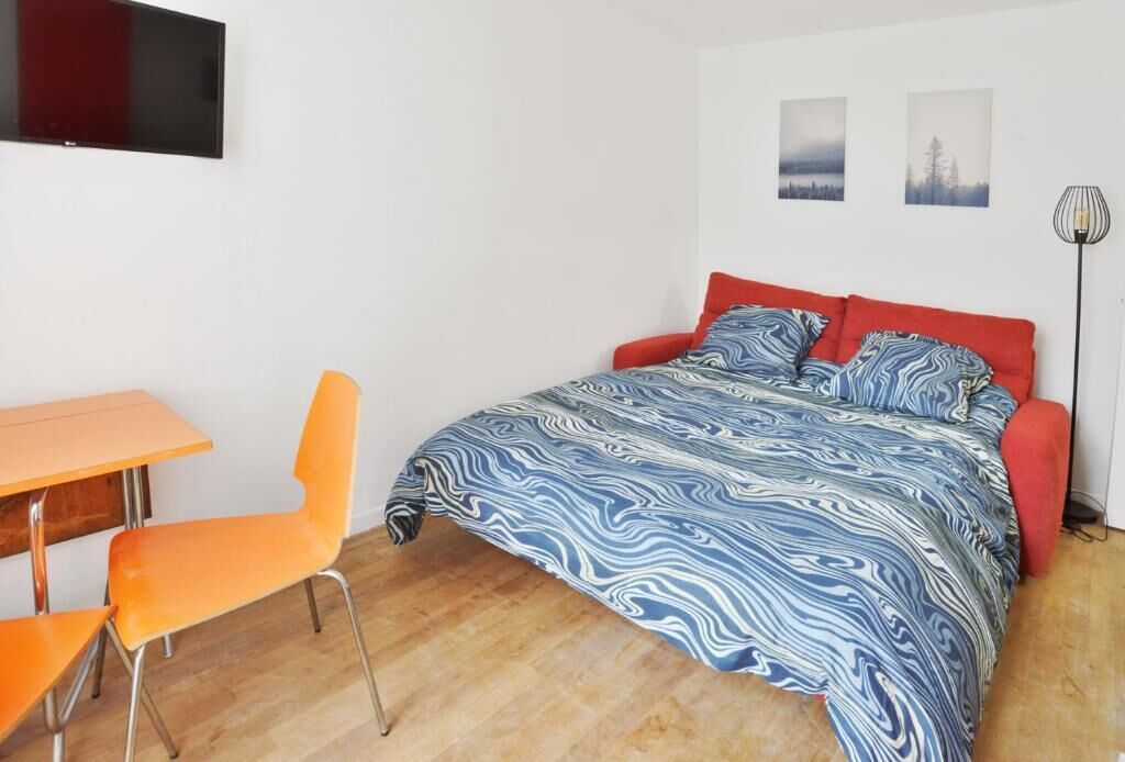 Een slaapkamer met een bed, een bureau en twee stoelen. Er hangen twee foto’s aan de muur en staat een vloerlamp.
