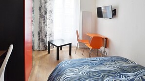 Une chambre d’hôtel équipée d’un lit, d’un bureau, d’une chaise, d’une télévision et d’une fenêtre avec des rideaux.